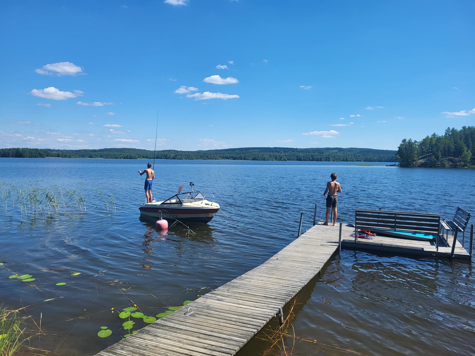 Wooden jetty with a small boat on a calm Finnish lake on a sunny summer day