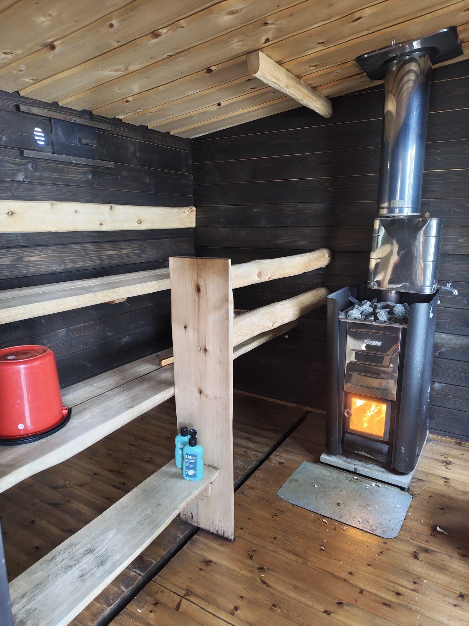 Wood-fired sauna interior with wooden benches and a burning stove