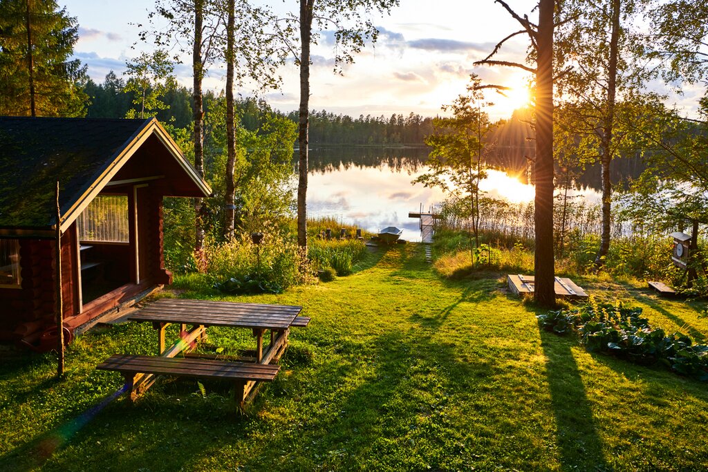Wooden lakeside building, picnic table and jetty among birches in Finland at sunset