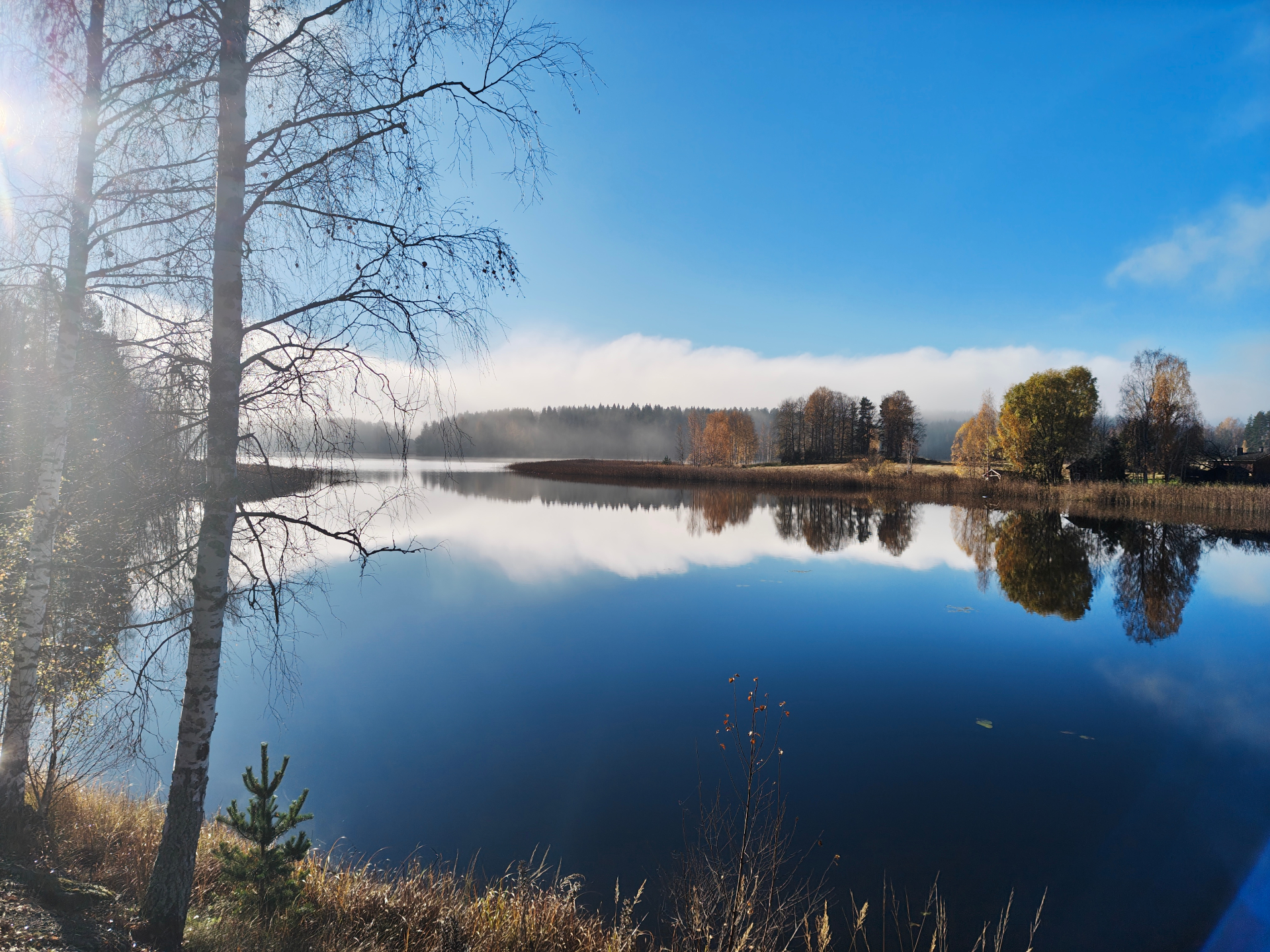 Calm, misty October morning on the lake in Luhanka, with autumn trees reflected in the water and a small red cottage among the trees in the background