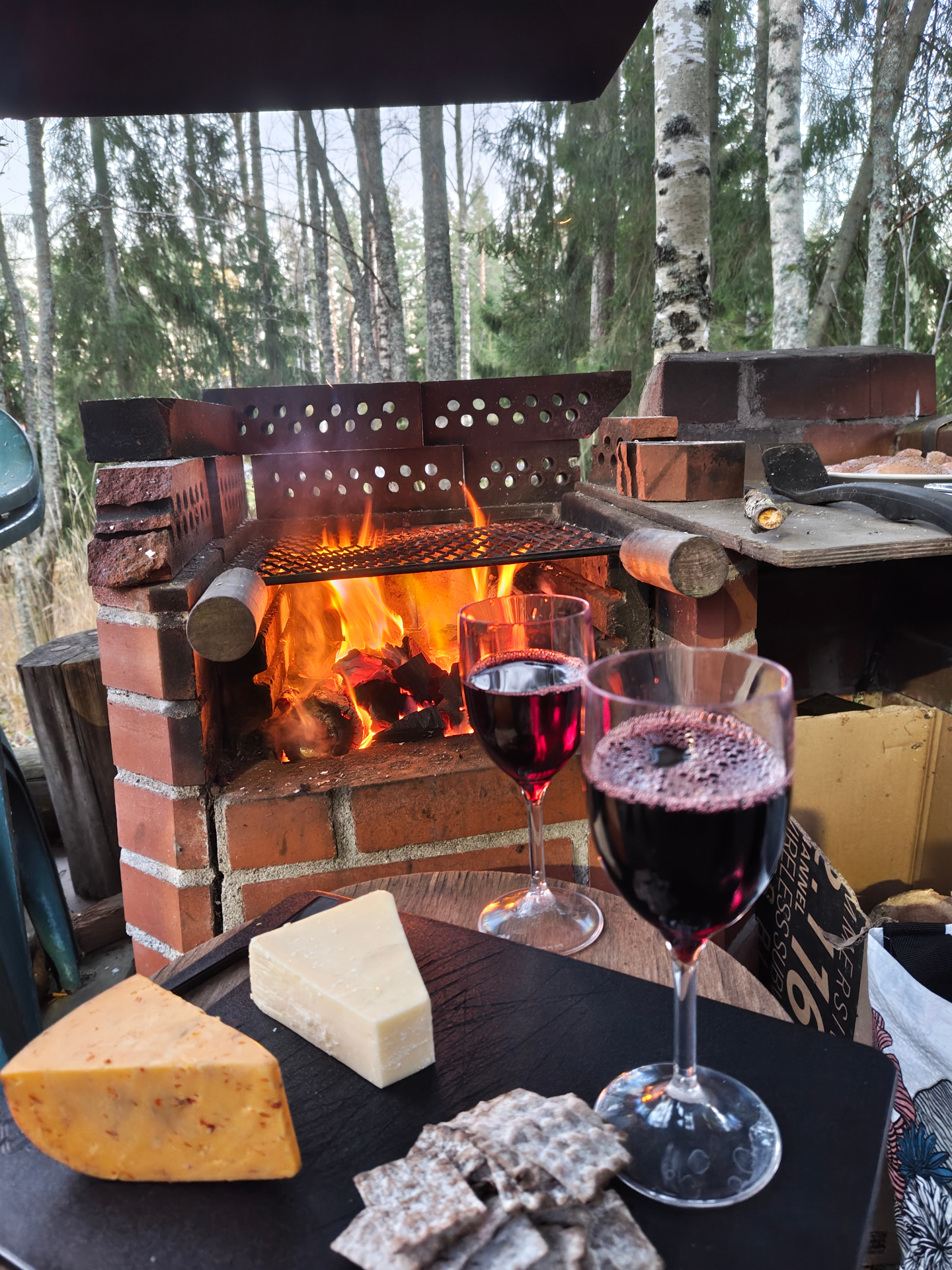 Flames in a brick outdoor fireplace on an autumn evening, with two glasses of red wine, cheese and crispbread