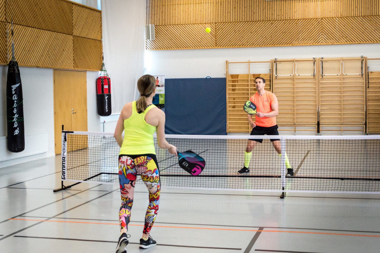 Two players in a pickleball rally on an indoor court