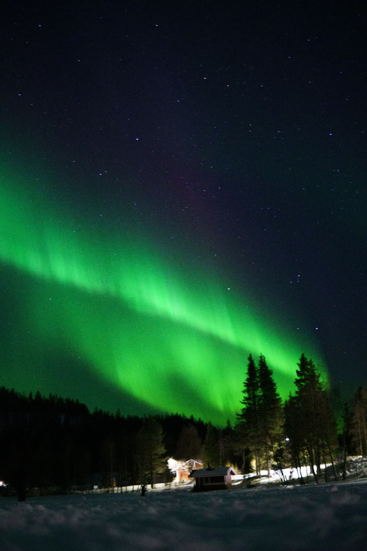 Snow-covered cabin in Finnish Lapland beneath subtle Northern Lights and a dark Arctic sky