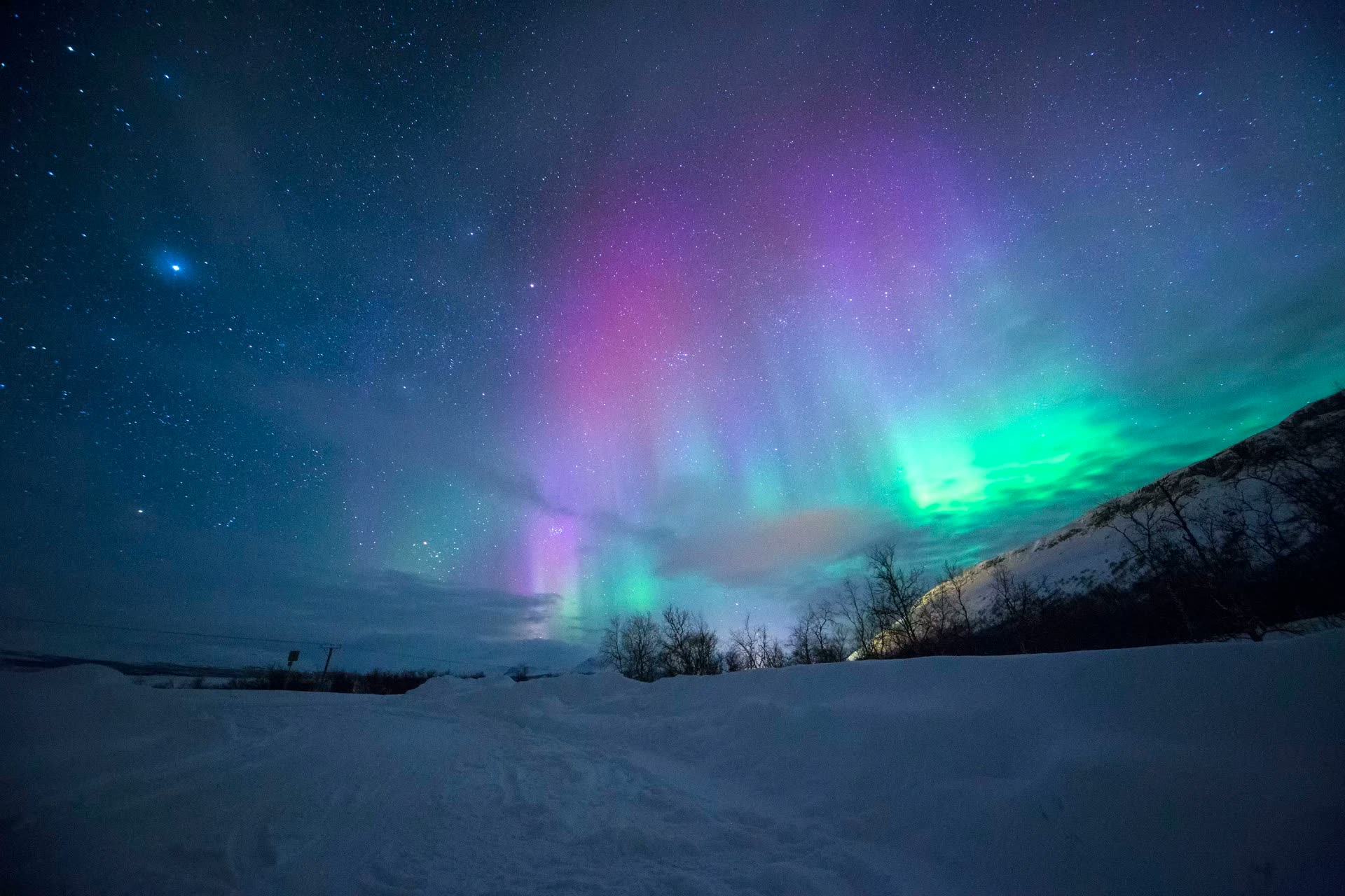 Snow-covered cabin in Finnish Lapland beneath subtle Northern Lights and a dark Arctic sky