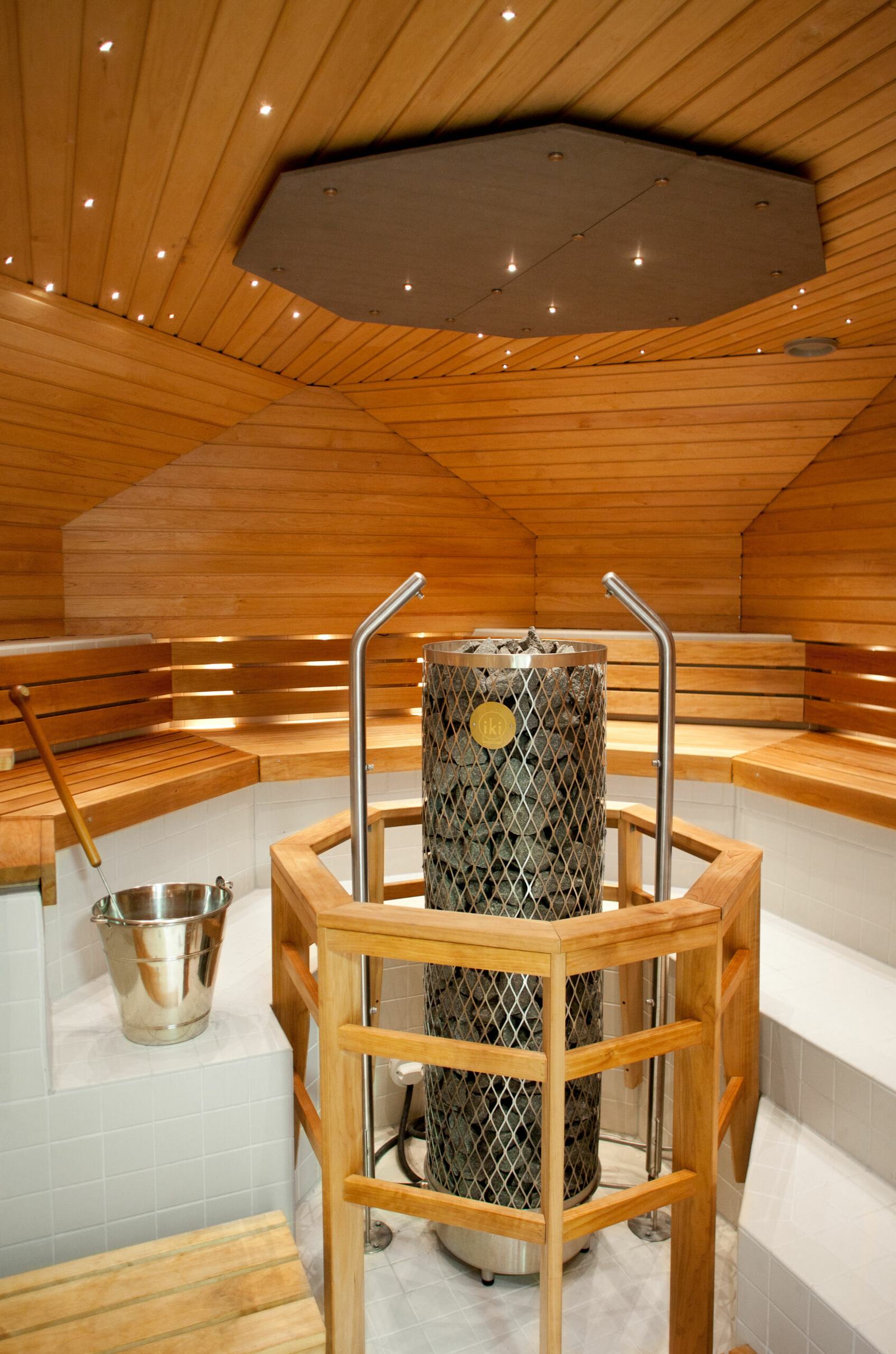 Water being thrown onto hot stones in a wood-heated Finnish sauna stove, steam rising in a wooden sauna room